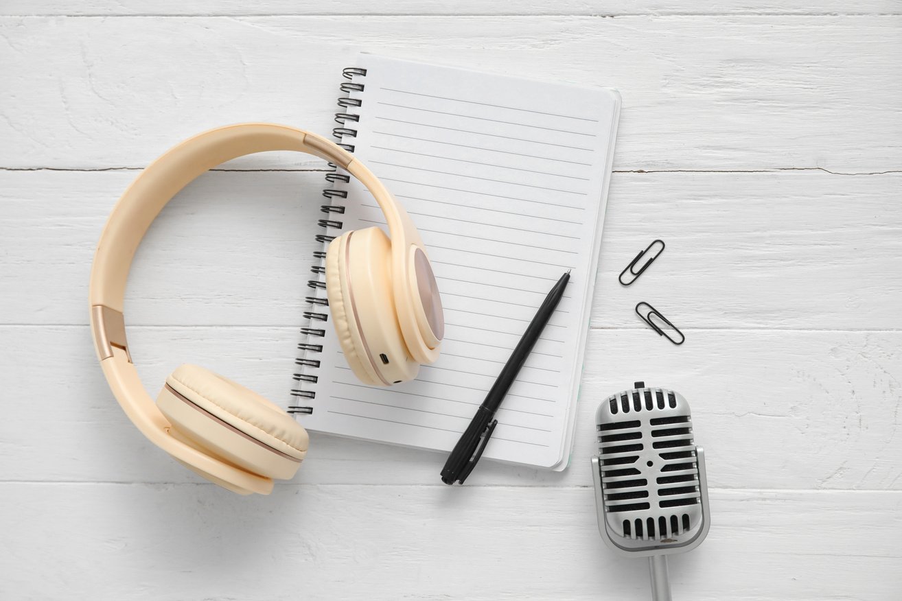 Notebook with Headphones, Paper Clips and Microphone on White Wooden Background. Podcast Concept